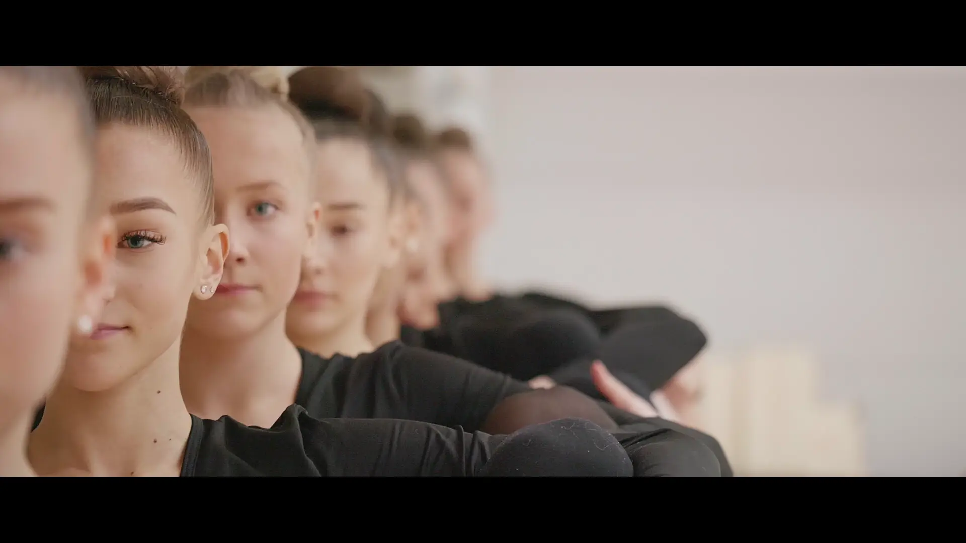 Lähikuva nuorten naisten kasvoista jonossa balettiasennossa, Espoolle tuotetussa videossa. Videolooppi.
