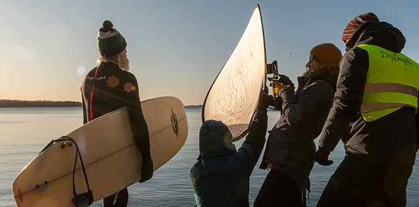 Behind the scenes Vanhusten keskusliitolle kuvatusta hankkeesta. Filmbutikin videokuvaajia, parrakas mies ja surffilauta.