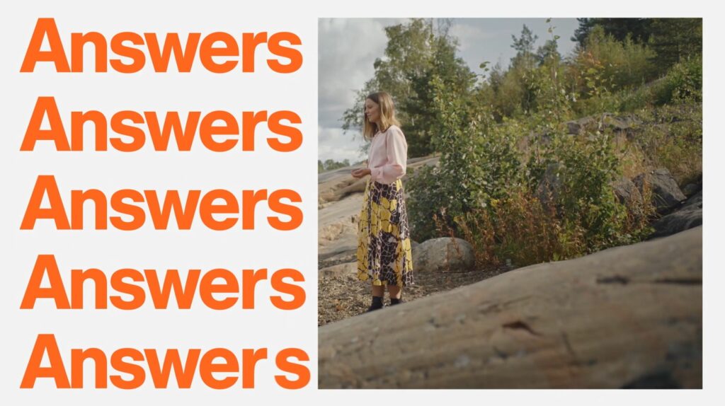 Vasemmalla oranssi answer teksti useasti päällekkäin. Oikealla nainen kalliolla. Taustalla metsää ja hän katselee eteenpäin.