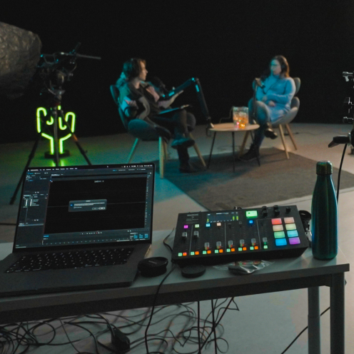 Kuva studiolta kun siellä on live stream kuvaukset. Edessä editointipöytä takana näkyy kaksi henkilöä pöydän ääressä.