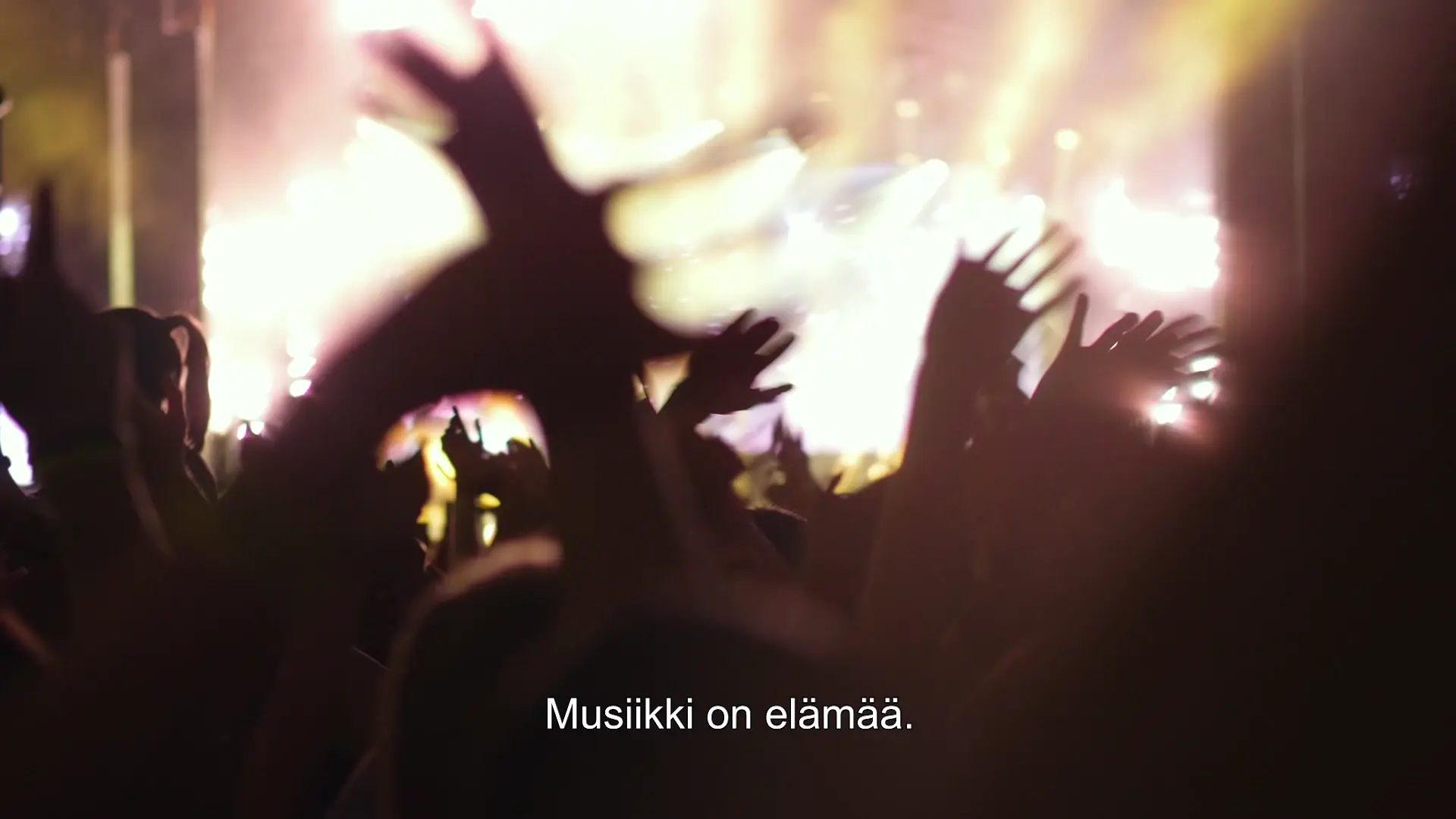 Paljon käsiä heiluu edestakaisin keikalla, lavan valot hohkavat kirkkaina. Video looppi.