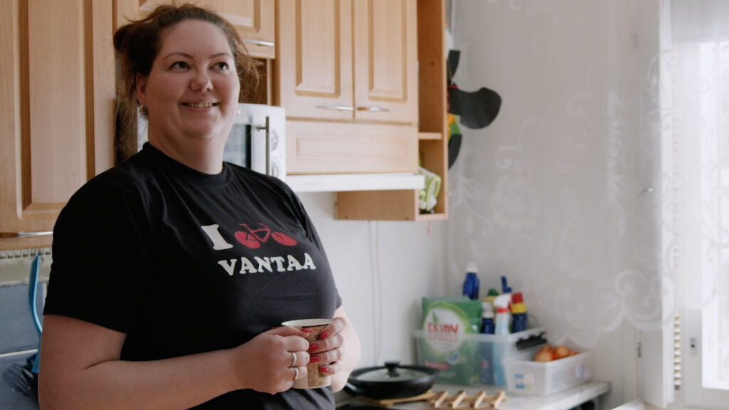 Hymyilevä nainen seisoo keittiössä, päällään musta t-paita jossa lukee Vantaa.