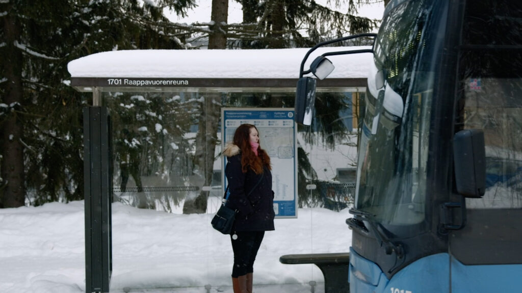 Nainen seisoo talvella bussipysäilla Vantaalla. Etualalla bussin etuosa.