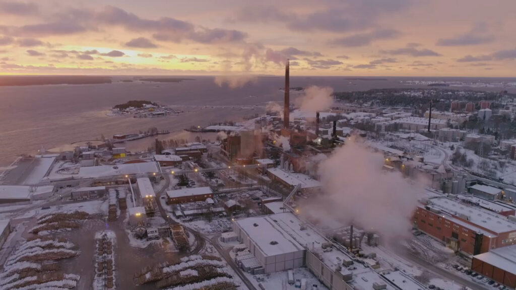 Talvinen kaupunki, jossa talojen katot lumessa ja meri jäässä. Aurinko pilkistää pilvien takana.