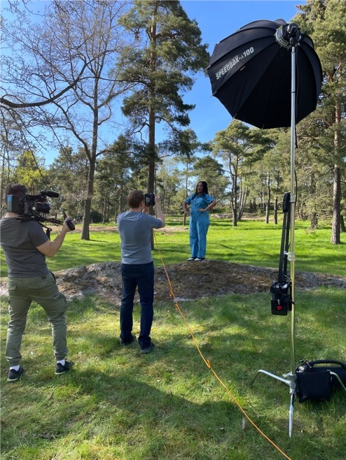Behind the scenes Yle:lle tutoetusta realitysarjasta. Kaksi kuvaajaa kuvaamassa naista, joka seisoo kalliolla puistossa.